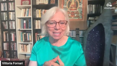 Vittoria in camicetta verde smeraldo sorride con le mani giunte nella sua biblioteca, tra il thangka del Buddha e un grande geode di ametista